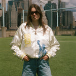 Woman wearing the FIFA souvenir jacket with jean shorts, standing on a soccer field. 