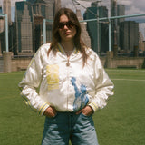 Woman wearing the FIFA souvenir jacket with jean shorts, standing on a soccer field. 
