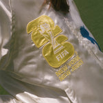 Close-up of a white jacket with FIFA logo and 'New York New Jersey' text on a grassy field.