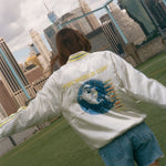Woman showing off the back of the souvenir jacket while standing on a soccer field. 