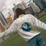 Woman showing off the back of the souvenir jacket while standing on a soccer field. 
