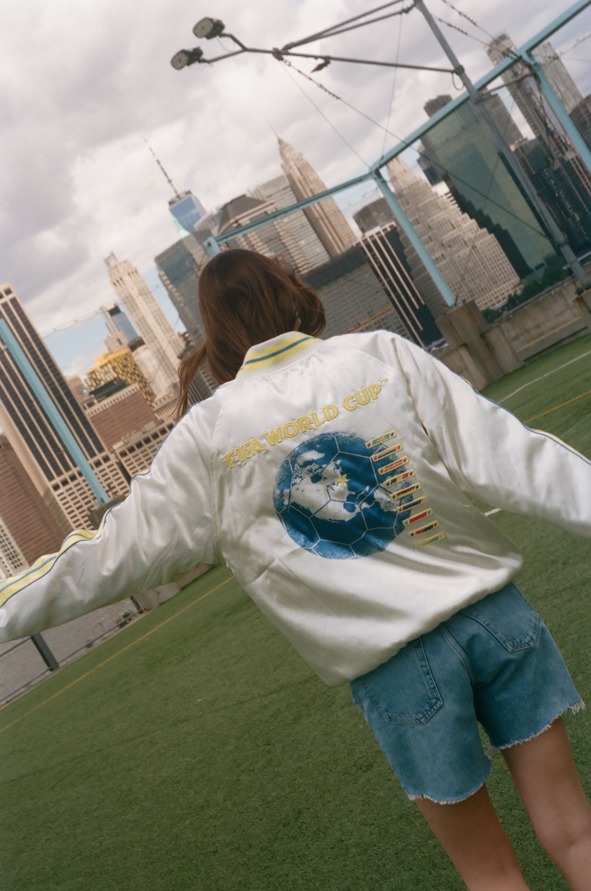Woman showing off the back of the souvenir jacket while standing on a soccer field. 