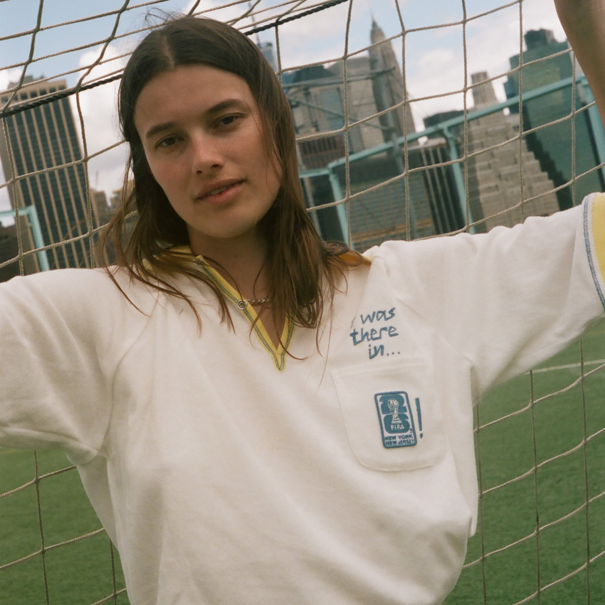 Woman wearing "Where were you?" FIFA Cabana shirt, leaning against a soccer net. 