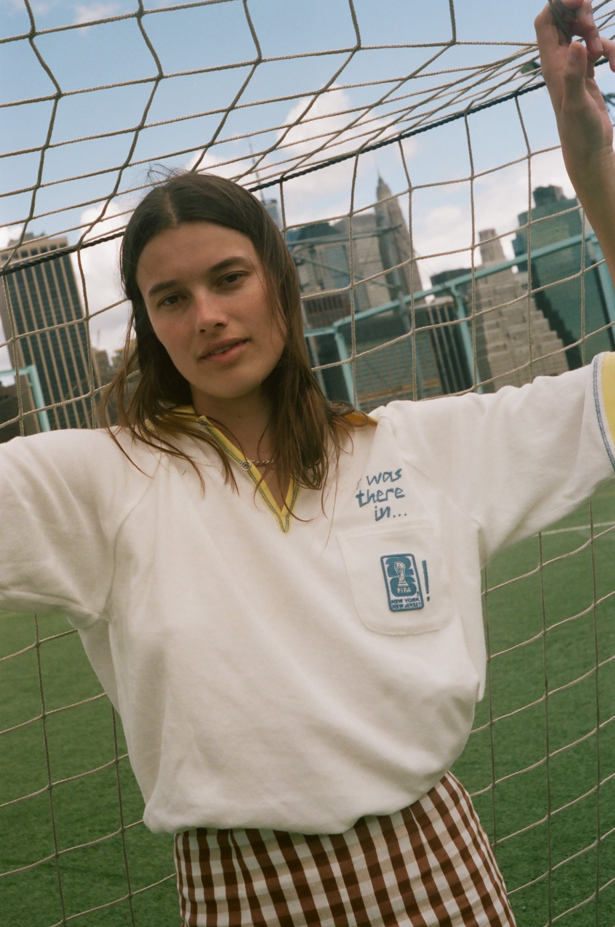 Woman wearing "Where were you?" FIFA Cabana shirt, leaning against a soccer net. 
