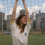 Woman hanging off the top of a soccer goal, wearing the 'Where were you?' Cabana from the FIFA and Tombolo collection.