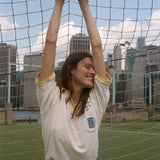 Woman hanging off the top of a soccer goal, wearing the 'Where were you?' Cabana from the FIFA and Tombolo collection.