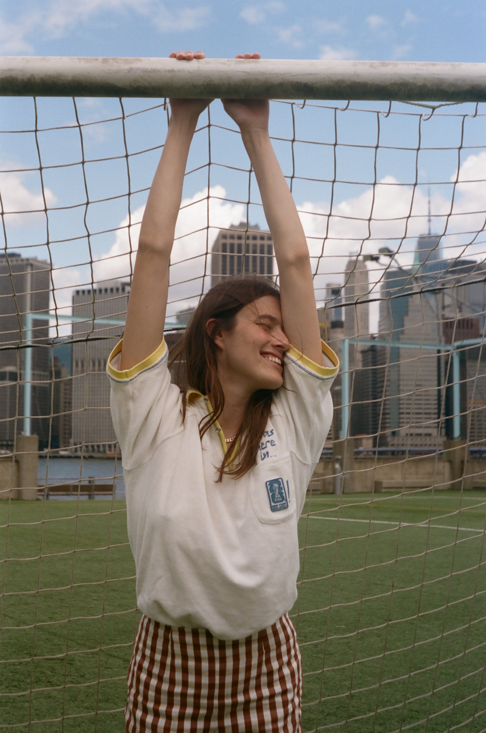 Woman hanging off the top of a soccer goal, wearing the 'Where were you?' Cabana from the FIFA and Tombolo collection.