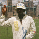 Person wearing a white terry cloth long sleeve shirt and bucket hat with city skyline in the background