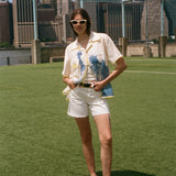 Woman in a white outfit with a blue statue of liberty design on her shirt for FIFA World Cup 2026 standing on grass with a city skyline in the background