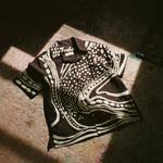 Black short sleeve cabana shirt with cream chain-stitch embroidery in a loon-inspired dotted and wave pattern, laid flat.