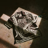 Black short sleeve cabana shirt with cream chain-stitch embroidery in a loon-inspired dotted and wave pattern, laid flat.