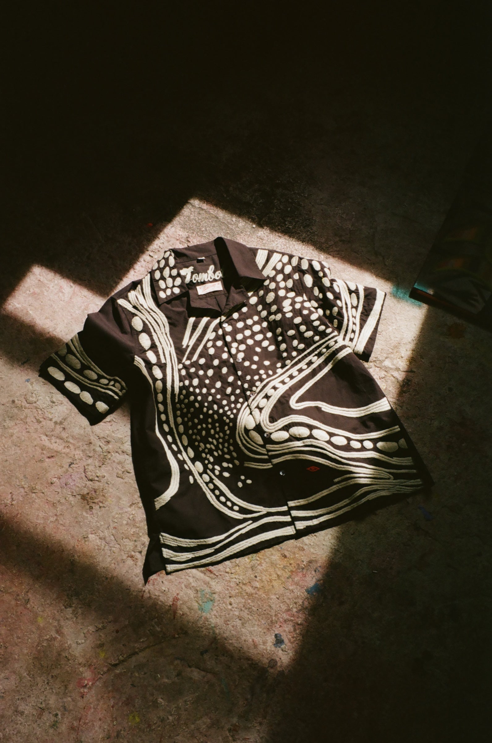 Black short sleeve cabana shirt with cream chain-stitch embroidery in a loon-inspired dotted and wave pattern, laid flat.