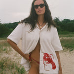 Woman wearing Lobster shirt oversized on the beach.