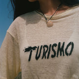 Close-up of 'Turismo' embroidery across a yellow linen tee.