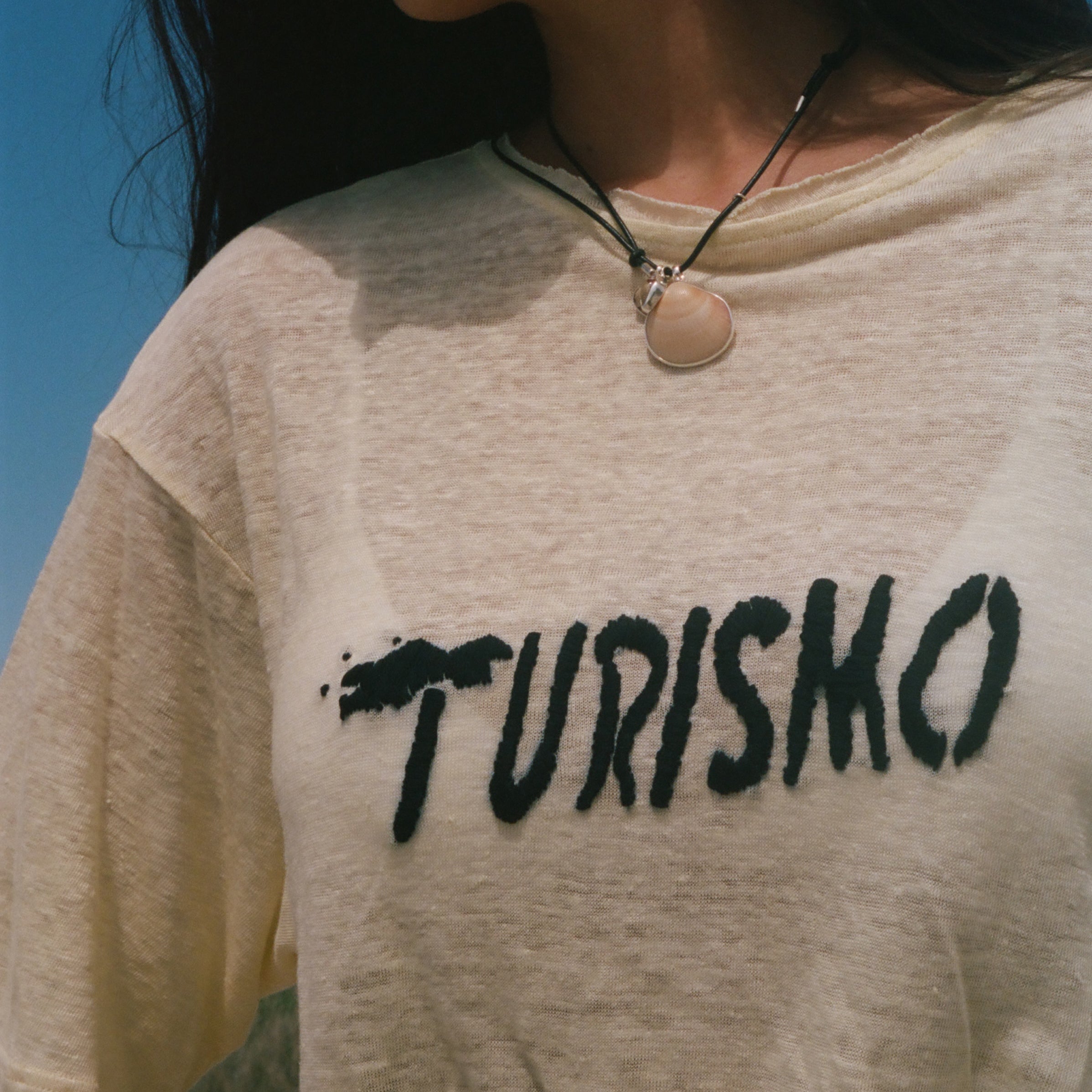 Close-up of 'Turismo' embroidery across a yellow linen tee.