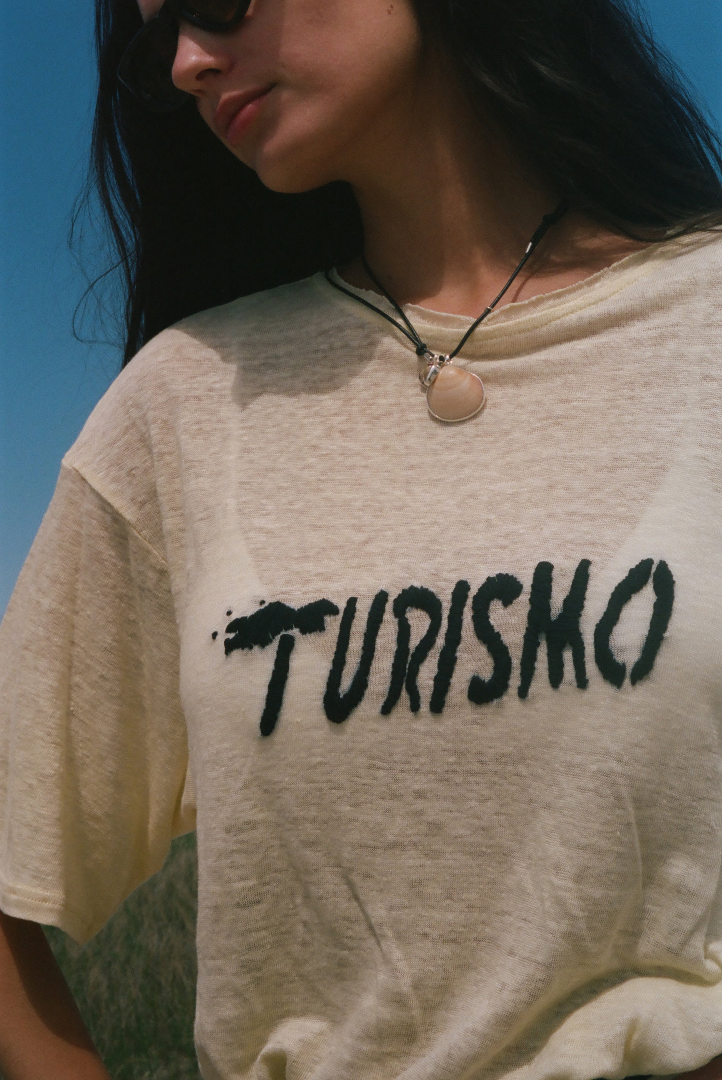 Close-up of 'Turismo' embroidery across a yellow linen tee.