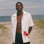 Man standing on a beach wearing a white terry shirt with a red lobster design on the front. 