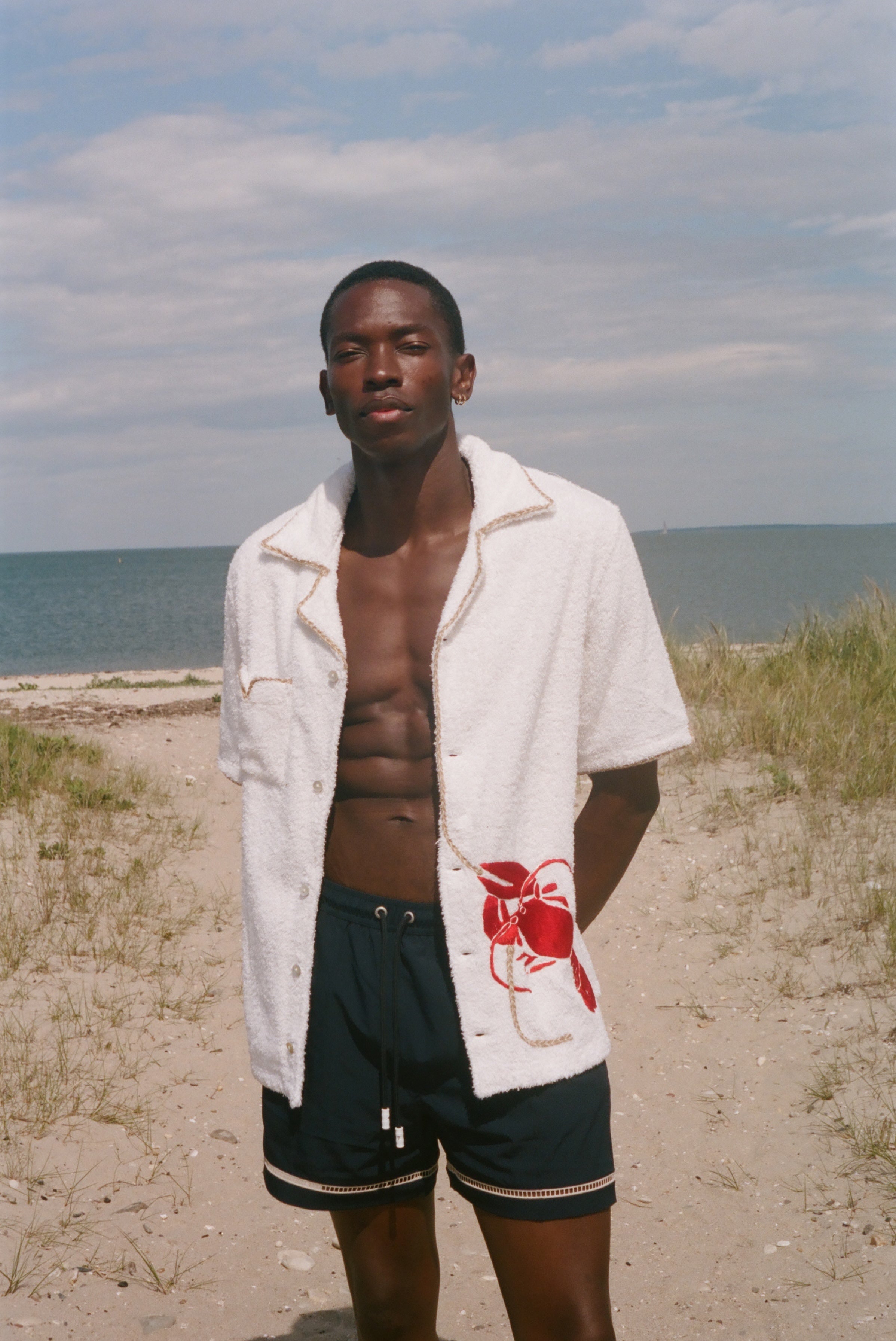 Man standing on a beach wearing a white terry shirt with a red lobster design on the front. 