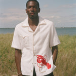 Man wearing a white shirt with a red lobster design in a grassy field 