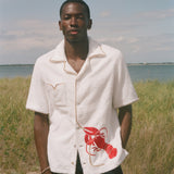 Man wearing a white shirt with a red lobster design in a grassy field 