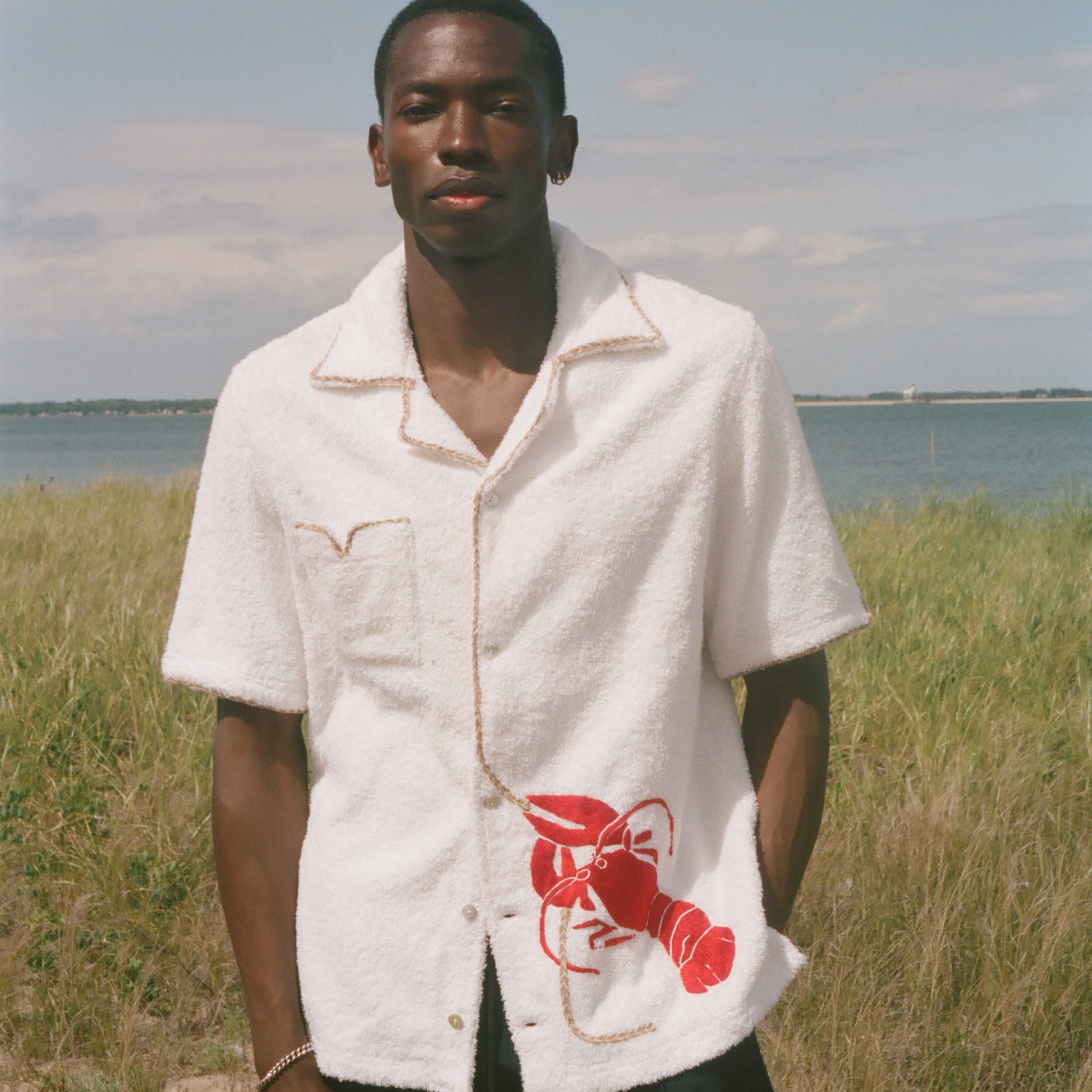 Man wearing a white shirt with a red lobster design in a grassy field 