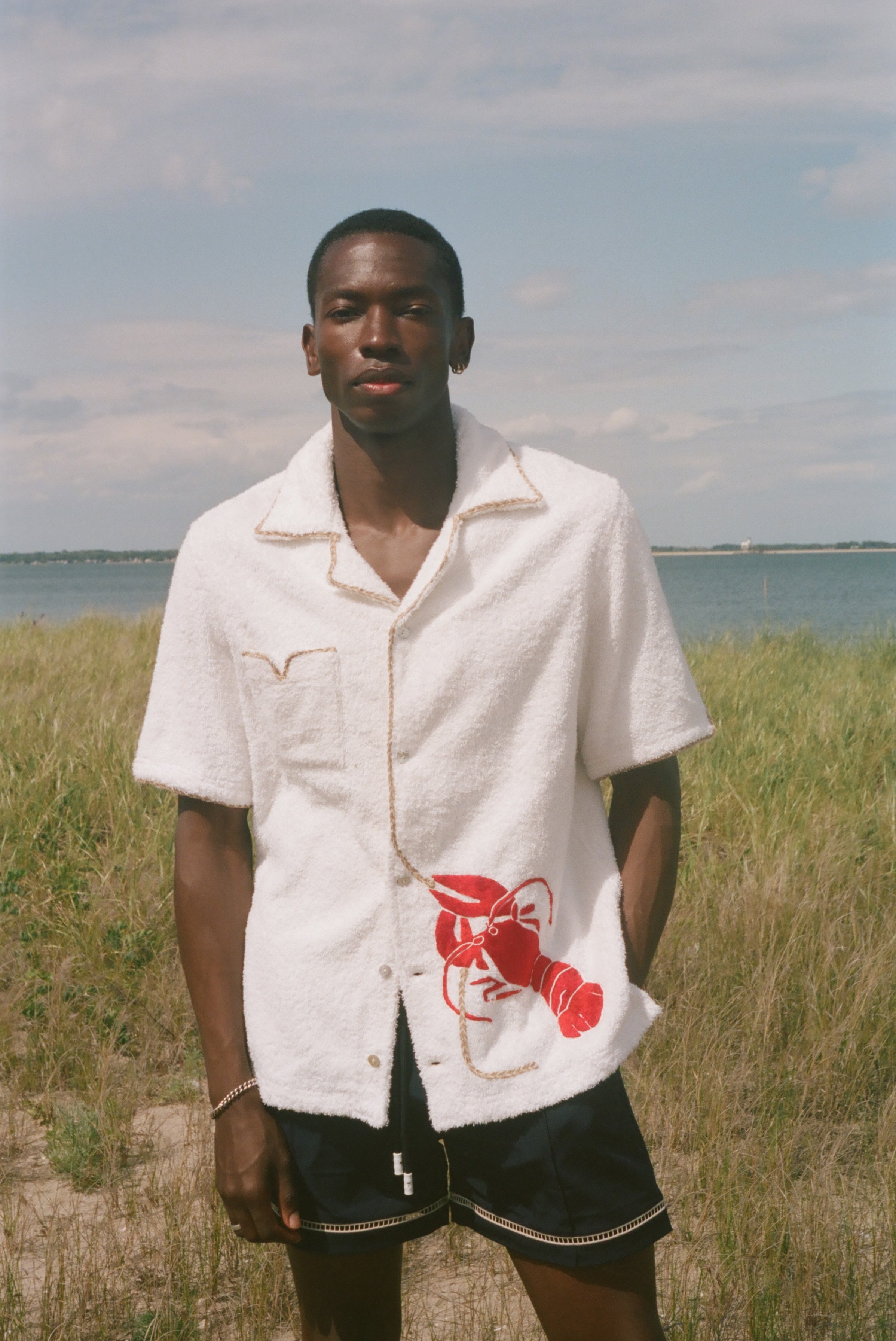 Man wearing a white shirt with a red lobster design in a grassy field 
