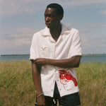 Man standing on a beach wearing a white terry shirt with a red lobster design on the front. 