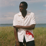 Man standing on a beach wearing a white terry shirt with a red lobster design on the front. 