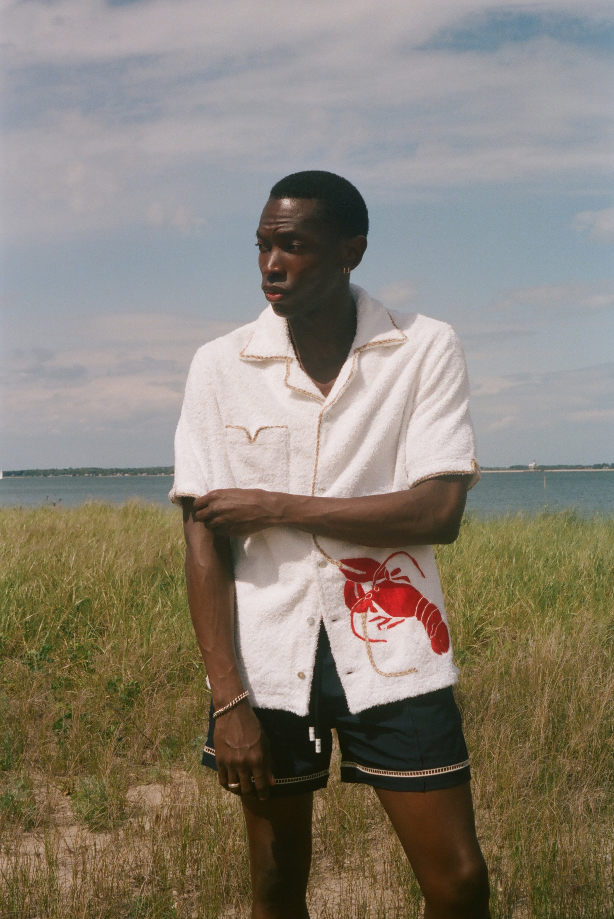 Man standing on a beach wearing a white terry shirt with a red lobster design on the front. 