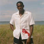 Man standing on a beach wearing a white terry shirt with a red lobster design on the front. 