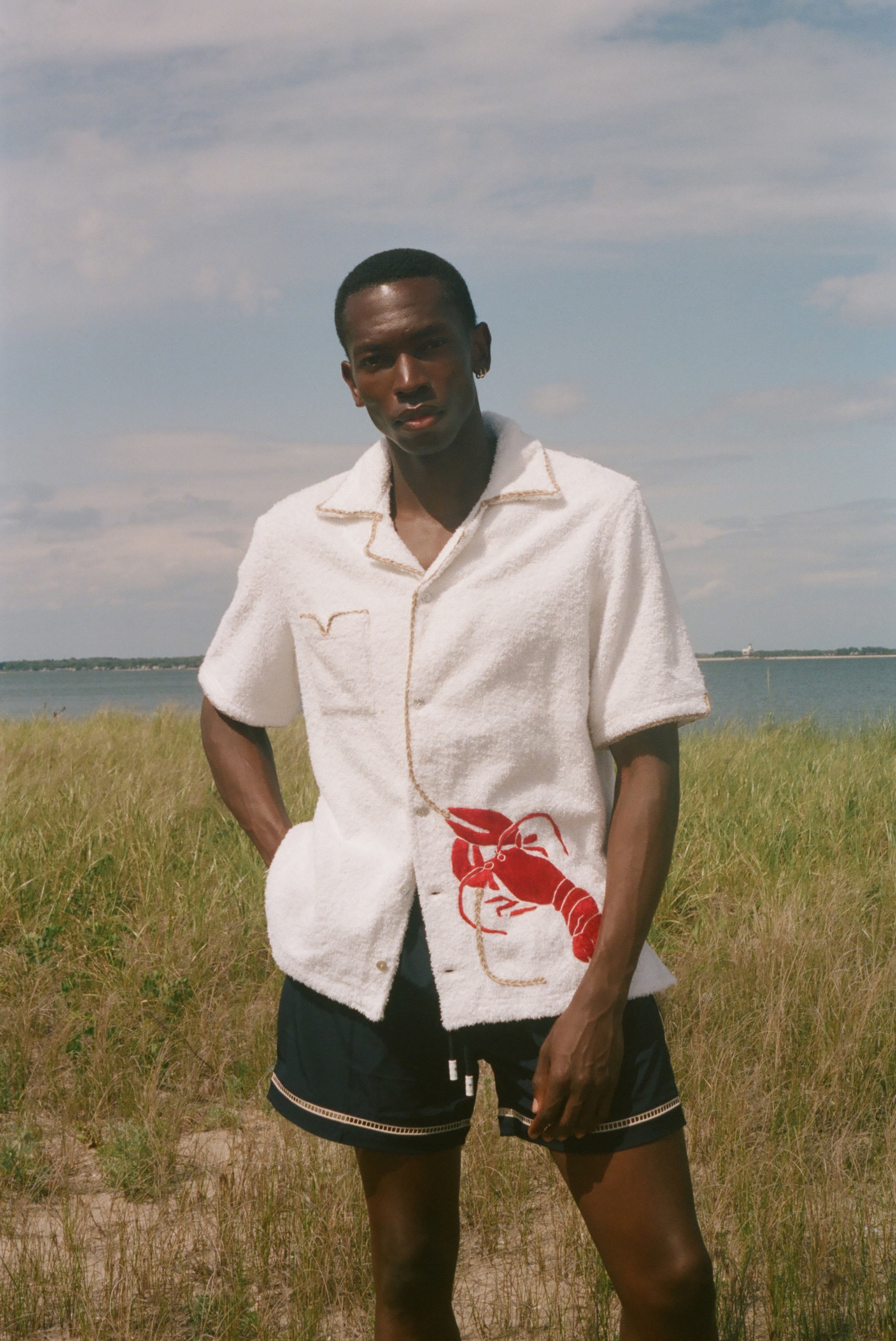 Man standing on a beach wearing a white terry shirt with a red lobster design on the front. 