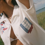 Close-up of a cream terry cabana shirt with embroidered floral vines and a blue shuttered window pocket detail.
