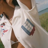 Close-up of a cream terry cabana shirt with embroidered floral vines and a blue shuttered window pocket detail.