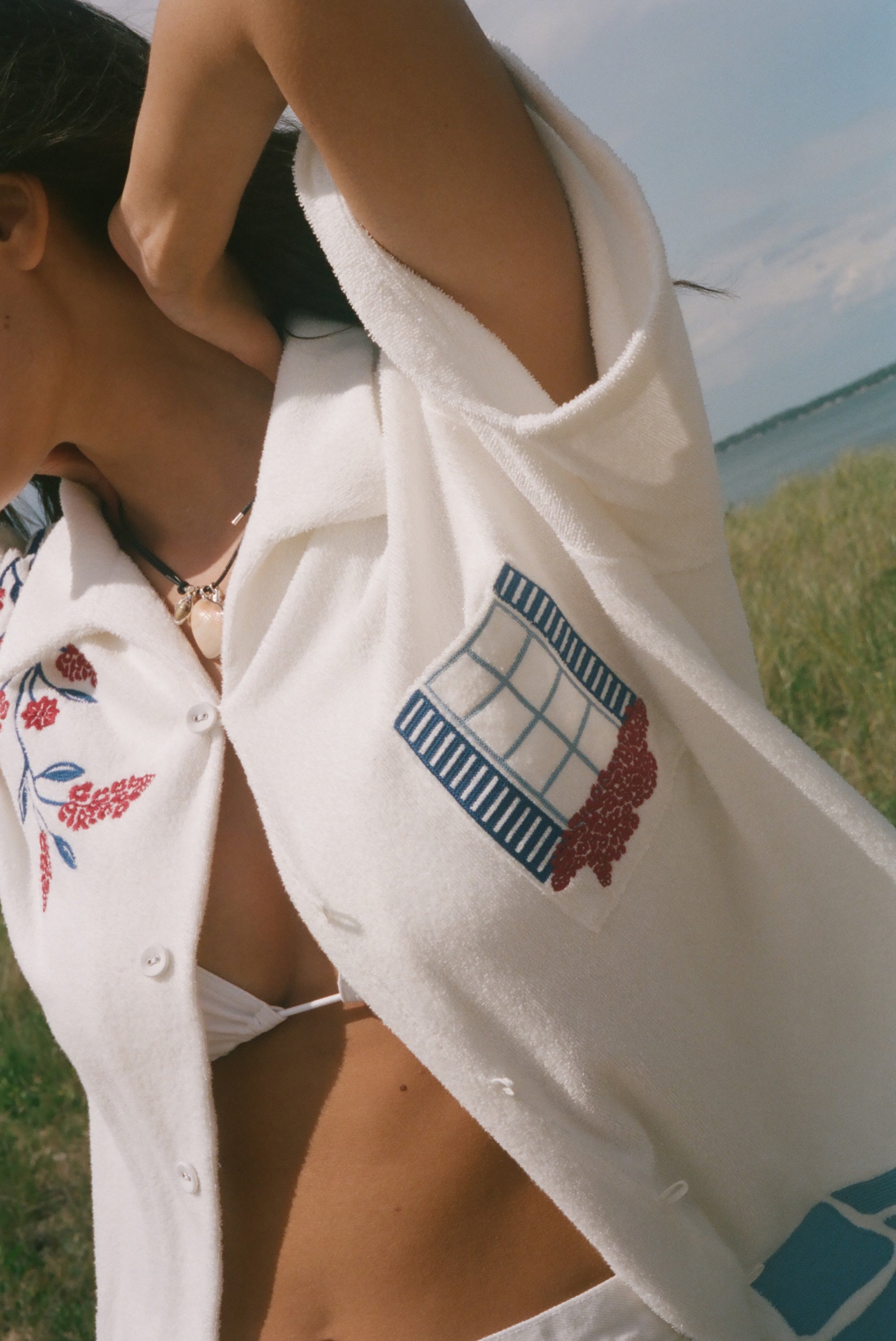 Close-up of a cream terry cabana shirt with embroidered floral vines and a blue shuttered window pocket detail.