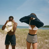 Two people on the beach putting on Tombolo cover ups. 