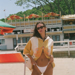 A woman posing on a sandy beach wearing a yellow and white patterned beach poncho.