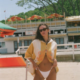 A woman posing on a sandy beach wearing a yellow and white patterned beach poncho.