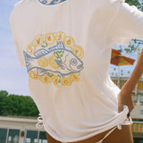 A woman wearing a white short-sleeve t-shirt with a graphic of a blue fish