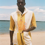 A man standing on a sandy beach wearing a yellow and off-white hooded poncho.