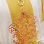Close-up of a yellow and white zip-up poncho featuring a large orange and blue graphic print on the front, worn by a person.