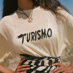 Woman wearing a yellow t-shirt with 'Turismo' text outdoors.