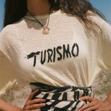 Woman wearing a yellow t-shirt with 'Turismo' text outdoors.