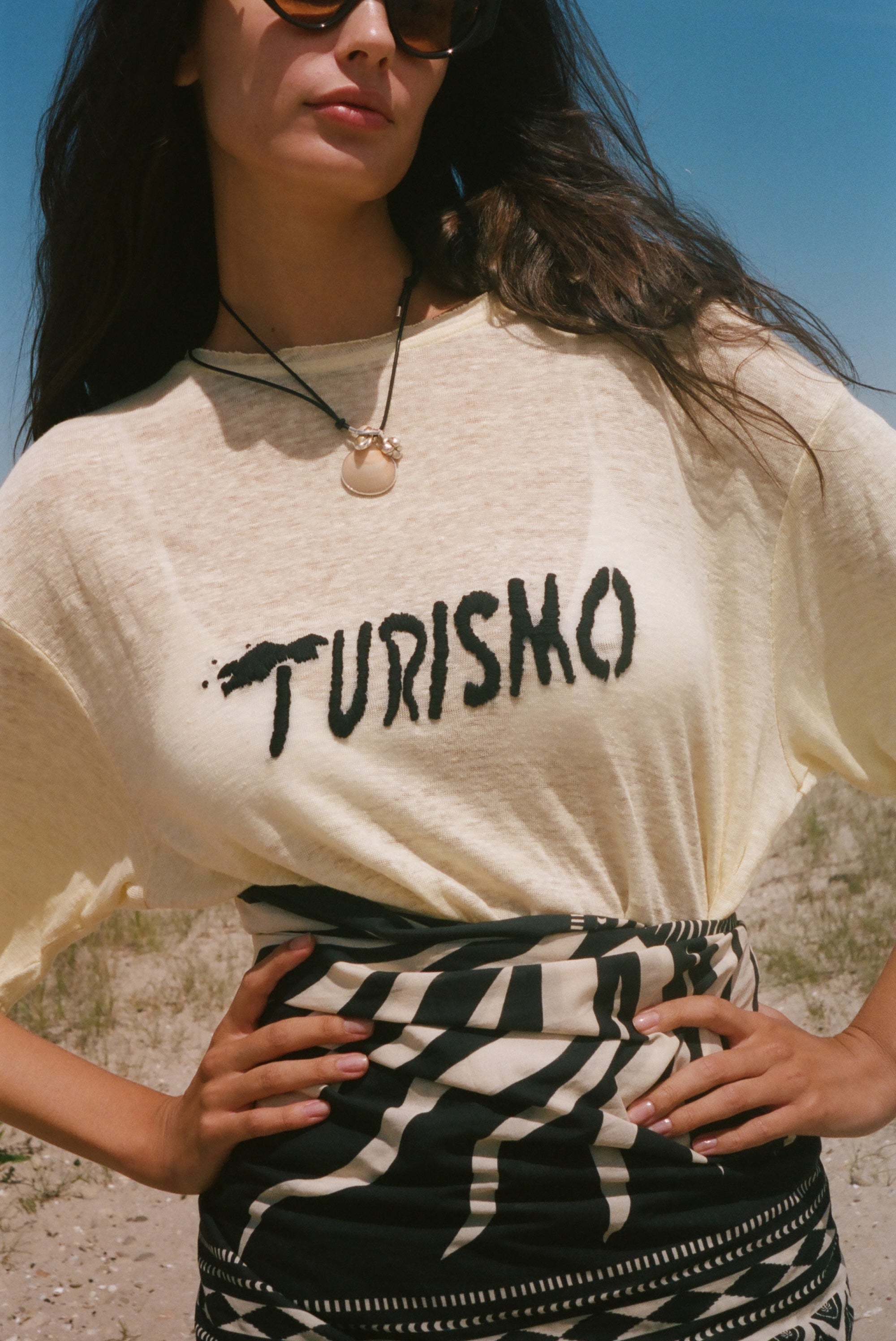 Woman wearing a yellow t-shirt with 'Turismo' text outdoors.