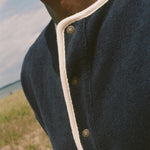 Close-up of a person outdoors wearing a dark navy knit henley shirt with cream trim and metal buttons.