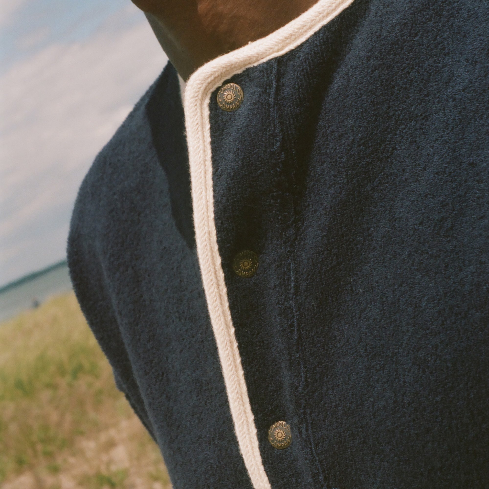 Close-up of a person outdoors wearing a dark navy knit henley shirt with cream trim and metal buttons.