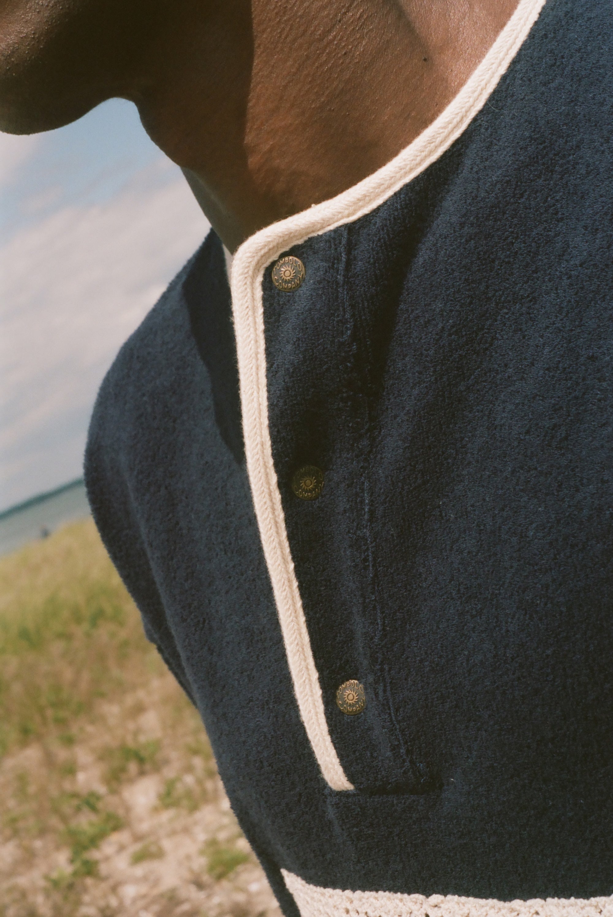 Close-up of a person outdoors wearing a dark navy knit henley shirt with cream trim and metal buttons.