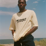 Man wearing a yellow t-shirt with 'Turismo' text on a beach
