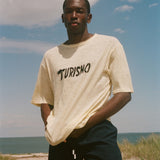 Man wearing a yellow t-shirt with 'Turismo' text on a beach