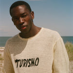 Man wearing a yellow t-shirt with 'Turismo' print on a beach
