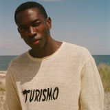 Man wearing a yellow t-shirt with 'Turismo' print on a beach